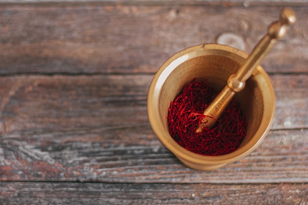 Épices de safran séché rouge organique brut sur table en bois dans un mortier en laiton métal vintage avec pilon.