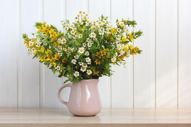 Pichet avec un bouquet d'été de fleurs de jardin sur une table sur un fond blanc