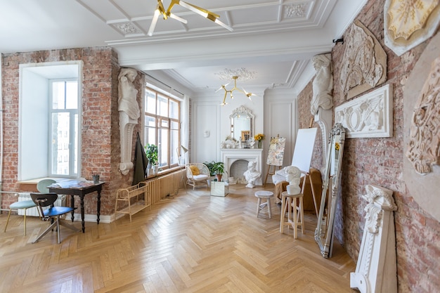 Pièce atelier lumineuse pour la création et le travail d'un architecte et artiste dans un style loft avec murs en briques et parquet. les murs sont décorés d'exemples de stuc.