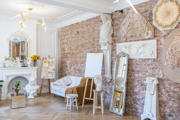 Pièce atelier lumineuse pour la création et le travail d'un architecte et artiste dans un style loft avec murs en briques et parquet. les murs sont décorés d'exemples de stuc.