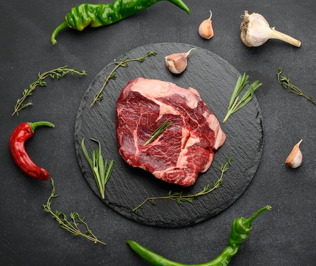 Pièce crue de faux-filet de boeuf au romarin, thym sur une table noire, vue de dessus