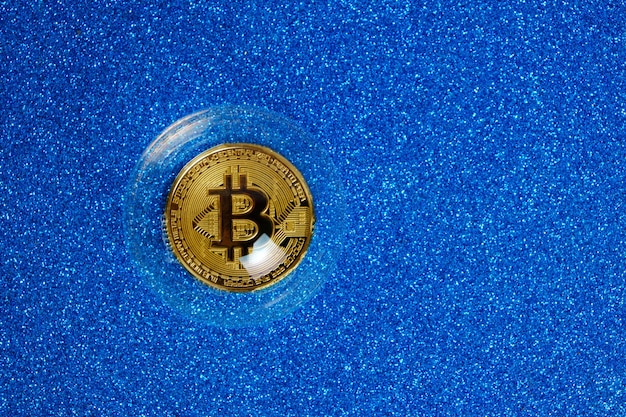Pièce de crypto-monnaie Bitcoin dans une bulle de savon sur fond bleu.