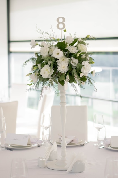 La pièce maîtresse faite de feuilles vertes et de fleurs fraîches se dresse sur la table du dîner.