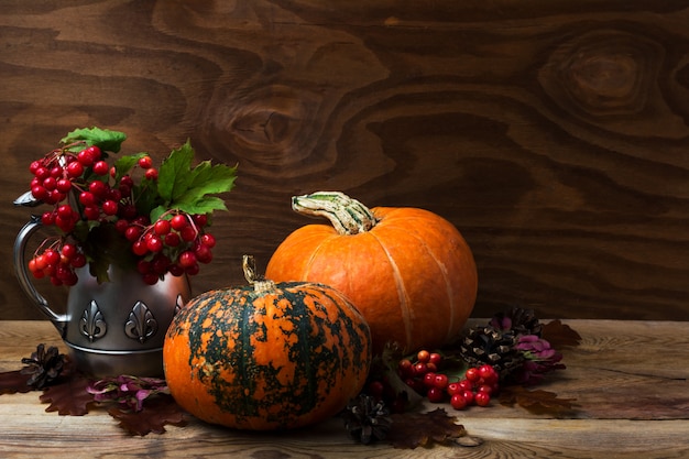 Pièce maîtresse de table rustique de Thanksgiving avec des baies de viorne rouge dans la bouilloire en argent antique et deux citrouilles orange, espace copie