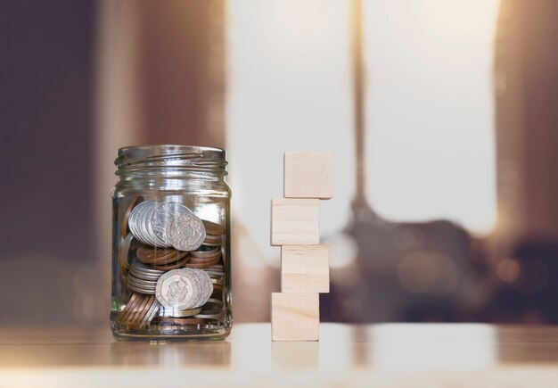 Pièce de monnaie sterling et pennies nickels en pot transparent avec maquette de pile vide en bois sur table avec arrière-plan flou.