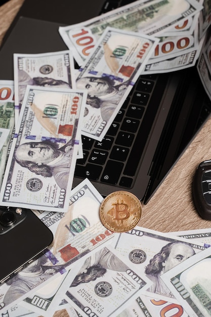 Pièce d'or bitcoin et dollars sur ordinateur portable sur la table d'un riche commerçant de crypto Riche investisseur avec une grande quantité de dollars en espèces et une pièce de monnaie en or bitcoin