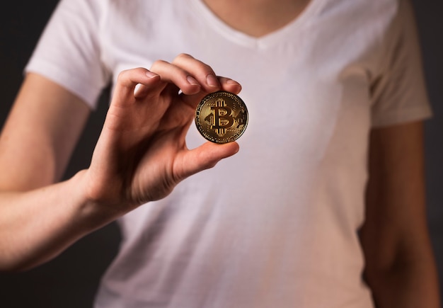 Pièce d'or de BTC ou bitcoin tenue par une main féminine.