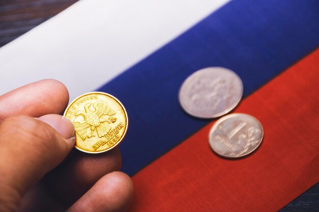 Pièce de rouble d'or sur la main et le drapeau de la Russie sur le fond