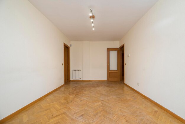 Pièce vide aux murs peints en blanc parquet en chêne point de Hongrie boiseries assorties et radiateur blanc