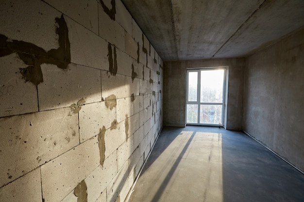 Pièce vide inachevée avec des murs de fenêtre en plastique faits de blocs de béton cellulaire et de chape de ciment au sol dans un bâtiment en construction