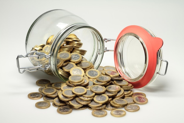 Des pièces d'euro renversées d'un récipient en verre sur un fond blanc