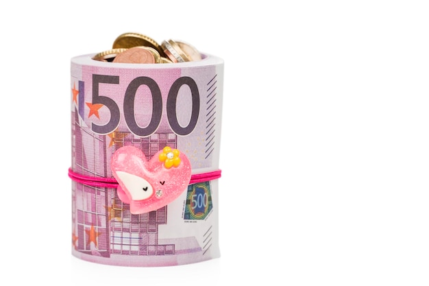 Pièces en euros dans une liasse de papier-monnaie d'une valeur nominale de cinq cents euros attachée avec une bande élastique avec un coeur isolé sur fond blanc.