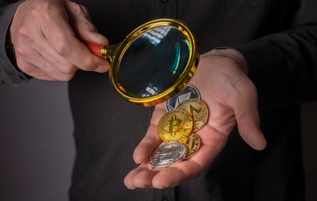 Pièces de monnaie de crypto-monnaie dans la main masculine avec gros plan de loupe tas de bitcoin et autre monnaie crypto