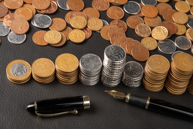 Pièces de monnaie, pièces de monnaie brésiliennes de divers montants entassés et un stylo plume sur cuir noir, mise au point sélective.