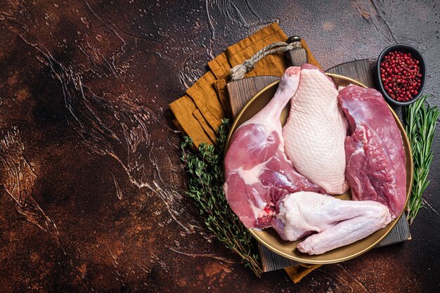 Pièces de viande de canard fraîches jambes de bifteck de poitrine crues ailes dans une assiette avec des herbes Fond sombre Vue de dessus Espace de copie