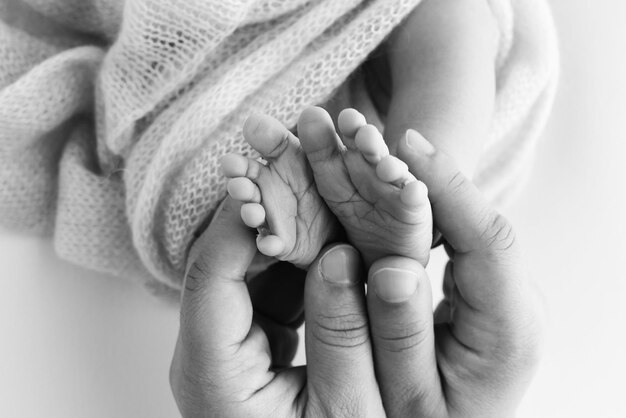 Le pied de l'enfant dans les mains de la mère, du père, des parents, les pieds d'un petit nouveau-né en gros plan, les petites jambes du bébé, la mère et son enfant, le concept de famille heureuse, l'image en noir et blanc de la maternité.