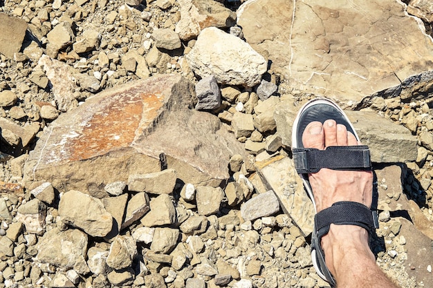 Pied de jeune homme en sandale noire de sport se dresse sur la plage de la mer couverte de rochers gris clair