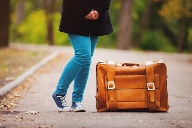 Pieds d'adolescent avec valise à l'automne en plein air.