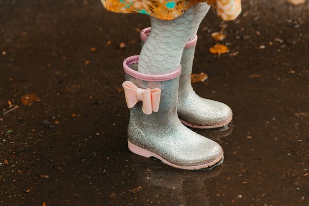 Photo pieds de bébé dans des bottes en caoutchouc se bouchent. l'enfant court dans les flaques d'eau un jour d'automne.