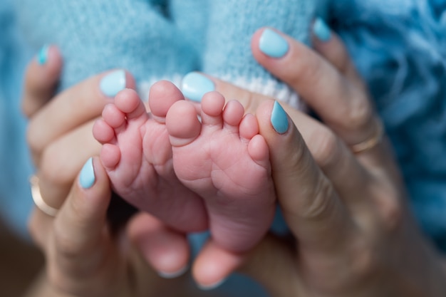 Les pieds de bébé dans les mains d'une femme aux ongles bleus