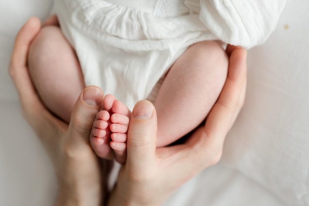 Pieds de bébé dans les mains de la mère sur fond blanc. Photographie de nouveau-né naturelle, blanche et simple