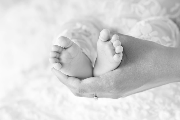 Pieds de bébé dans les mains de la mère Petits pieds de bébé nouveau-né sur les mains en forme de femme agrandi Maman et son enfant Concept de famille heureuse Belle image conceptuelle de la maternité Image en noir et blanc