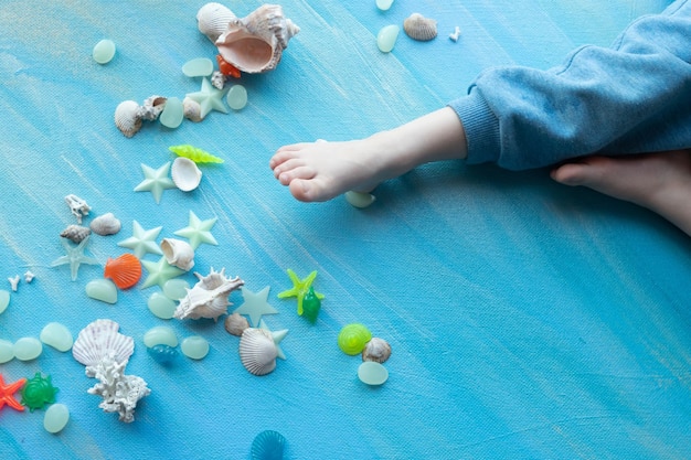 Pieds de bébé sur fond d'été de coquillages Beaucoup d'étoiles de mer de coquillages différents sur un fond de traits de peinture bleu Place pour le texte