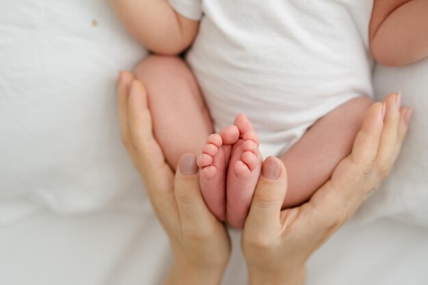 Pieds de bébé nouveau-né dans les mains de la mère sur fond blanc. Tenir dans le concept des mains. Idée de portrait de famille