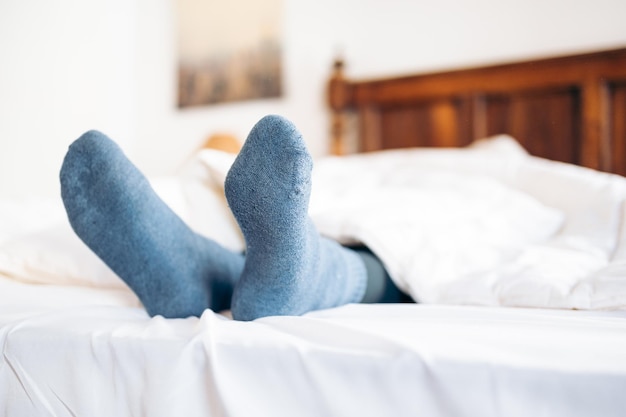 Pieds avec des chaussettes bleues qui sortent de sous la couette au lit