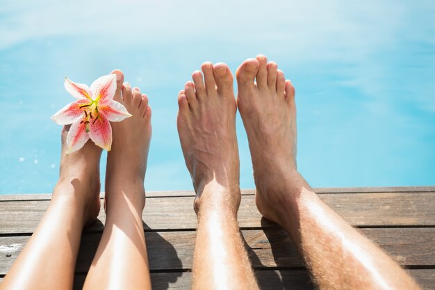 Pieds de couple contre la piscine par une journée ensoleillée