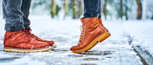 Pieds d'un couple sur un trottoir enneigé en bottes marron