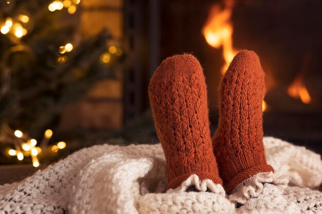 Pieds dans des chaussettes en laine près de la cheminée pendant les vacances d'hiver. Repos près de la cheminée à l'intérieur, gros plan.