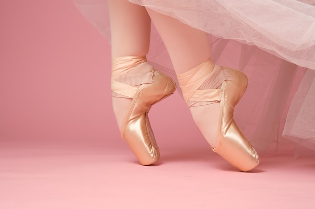 Pieds de danseuse de ballet classique en bas et jupe blanche sur la pointe des pieds avec des chaussures de pointe de ballet sur fond rose