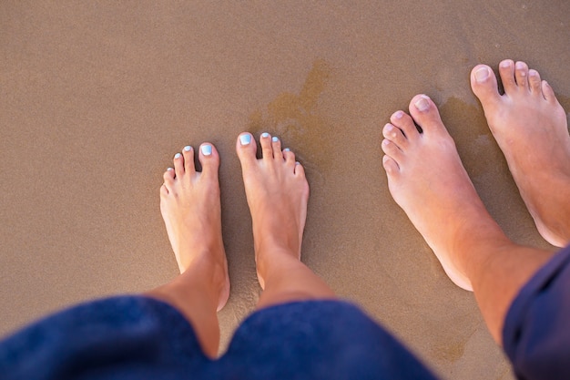 Pieds de deux amoureux sur le sable-été, soleil, mer, plage.