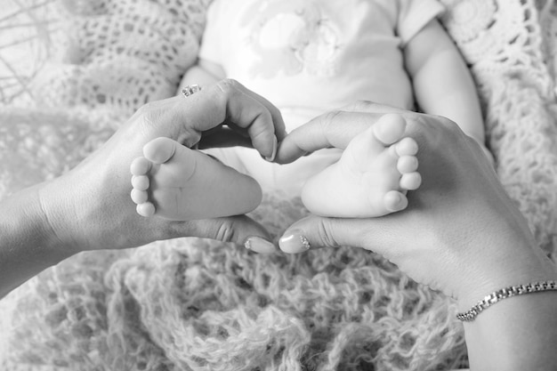 Les pieds du bébé nouveau-né dans les mains de la mère forment comme un joli coeur Mère tenant les jambes de l'enfant dans les mains