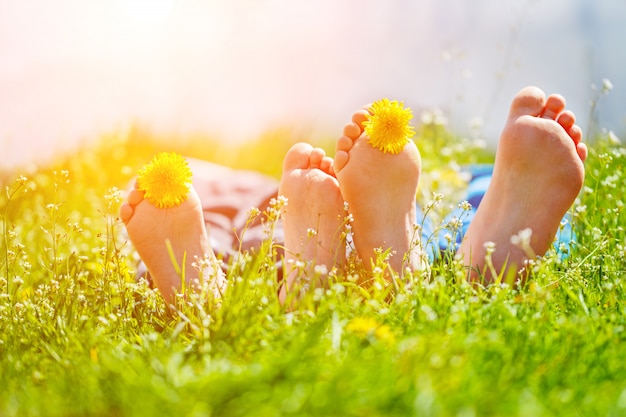 Pieds d&#39;enfants avec des fleurs de pissenlit, couché sur l&#39;herbe verte en journée ensoleillée. Concept enfance heureuse.