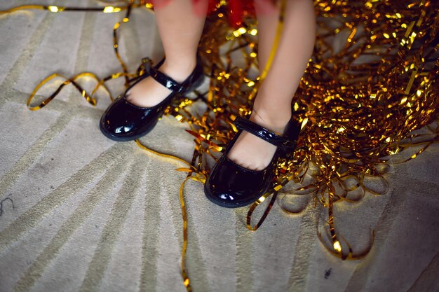 Photo les pieds d'enfants en sandales noires se tiennent sur un tapis avec des rubans de décoration en or à proximité