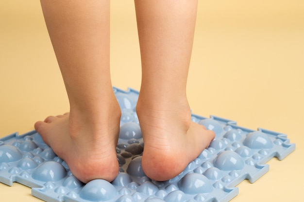 Pieds d'enfants sur un tapis orthopédique bleu sur fond beige traitement et prévention des pieds plats