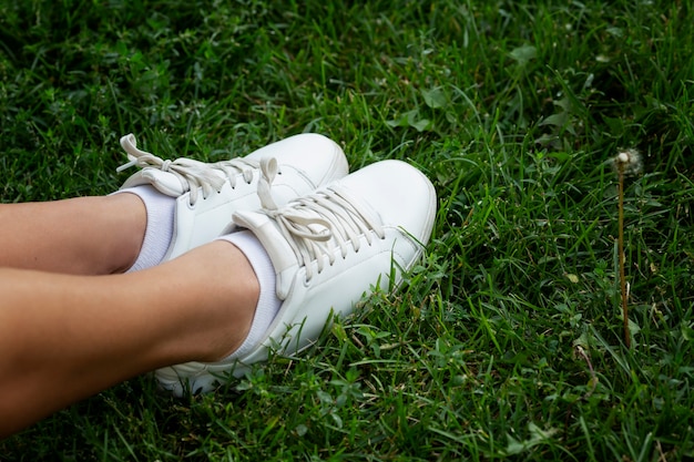 Pieds féminins en baskets blanches sur l'herbe verte. Activité et détente pendant la saison chaude.