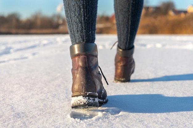 Pieds féminins en bottes s'éloignant sur la neige fraîche en hiver. Gros plan de chaussures d'hiver.