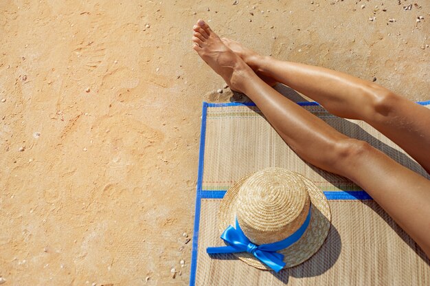 Pieds féminins et un chapeau de paille contre la mer sur la plage d&#39;été