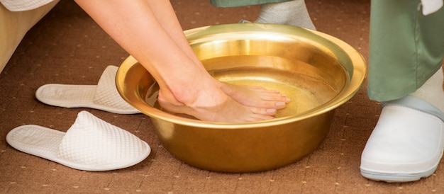 Pieds féminins dans un bol doré avec de l'eau dans un salon spa. Traitement de Spa.