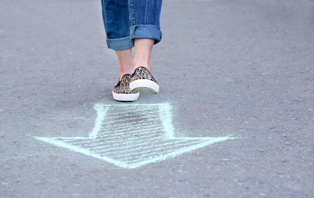 Pieds féminins et flèche de dessin sur fond de chaussée