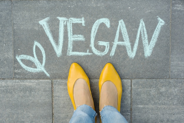 Pieds féminins avec texte végétalien écrit sur le trottoir gris