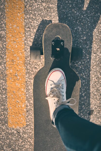 Pieds de femme en baskets sur un longboard le soir