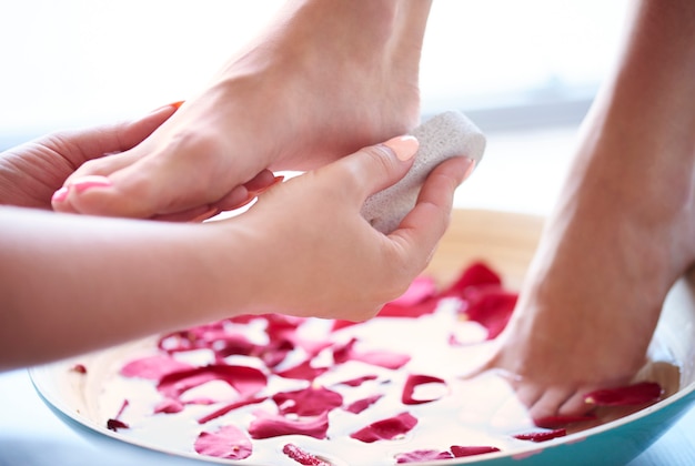 Pieds de femme dans un bol avec de l'eau et des pétales