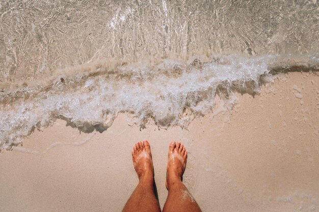 Les pieds de la femme se tiennent près des vagues de la mer sur la plage rose