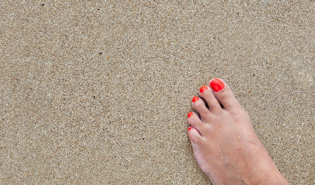 Photo des pieds de femmes avec une pédicure dans le sable sur la plage en gros plan