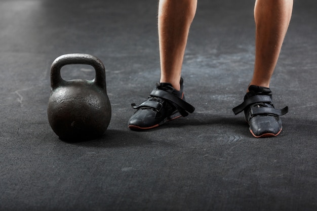 Pieds d'homme en baskets noires avec kettlebell noir en gymnastique