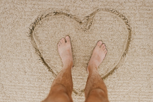 Pieds d'hommes au coeur sur le fond et le sable clair